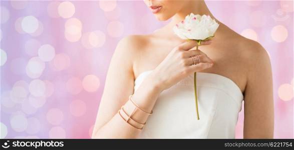 glamour, beauty, jewelry and luxury concept - close up of beautiful woman with golden ring and bracelet holding flower over pink holidays lights background