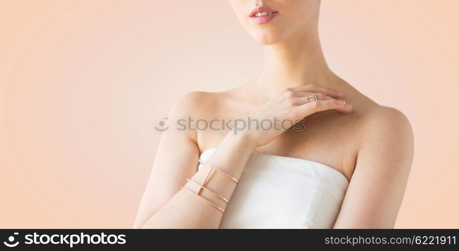 glamour, beauty, jewelry and luxury concept - close up of beautiful woman with golden ring and bracelet over beige background