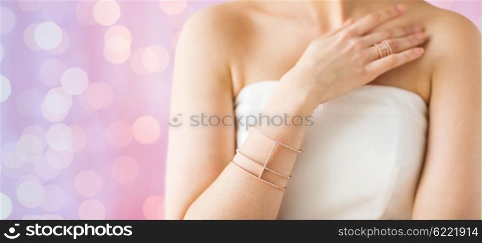 glamour, beauty, jewelry and luxury concept - close up of beautiful woman with golden ring and bracelet over pink holidays lights background