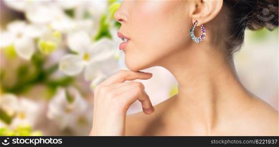 glamour, beauty, jewelry and luxury concept - close up of beautiful woman face with earring over natural spring lilac blossom background