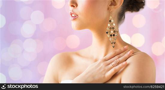 glamour, beauty, jewelry and luxury concept - close up of beautiful woman with earrings over pink holidays lights background