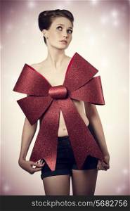 glamour christmas portrait of sexy girl with elegant hair-style, posing with big red bow on her naked breast, adorned like a present