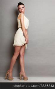 Glamour girl in white dress on gray. Fashion young slim woman posing in full length. Studio photo