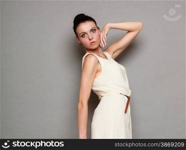 Glamour girl in white dress on gray. Fashion young woman hait bun posing. Studio photo