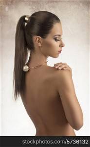 glamour woman with golden accessory posing with naked back, smooth ponytail hair-style and stylish make-up