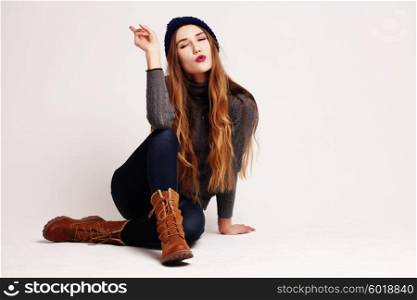 Glamourous portrait of the young beautiful woman in leather boots and autumn clothes posing over white background, sitting on the floor. Studio shot. Hipster style.