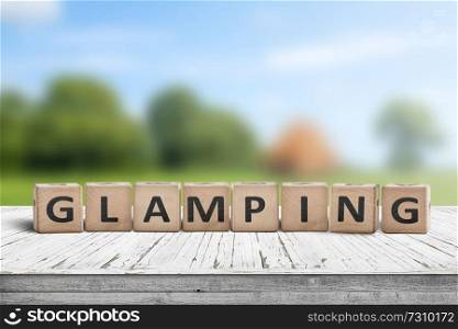 Glamping sign on wooden planks in the summer with a green camping area in the background