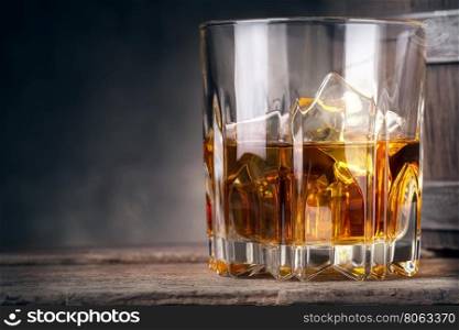 Glare glass of whiskey with ice and barrel in the background. Glare glass of whiskey with ice