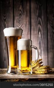 Glass and a mug of light beer with foam and ears on the wooden background. Glass and a mug of light beer with foam and ears