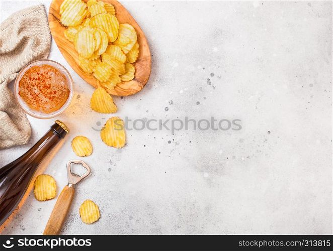 Glass and bottle of craft lager beer with potato crisps snack and opener on stone kitchen table background. Beer and snack.