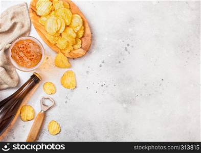 Glass and bottle of craft lager beer with potato crisps snack and opener on stone kitchen table background. Beer and snack.