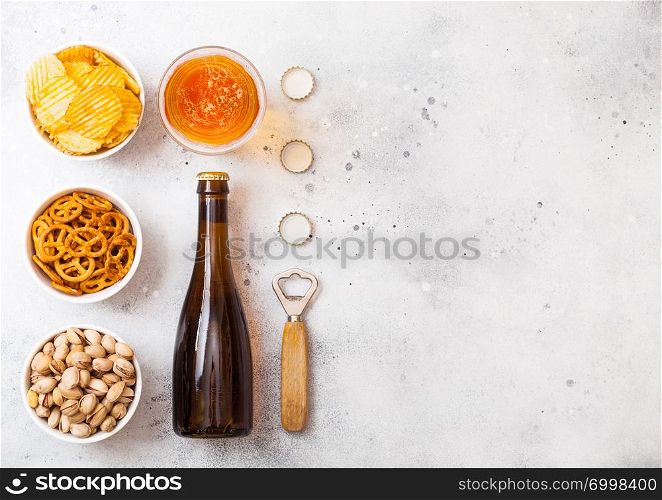 Glass and bottle of craft lager beer with snack on stone kitchen background. Pretzel and crisps and pistachio in white ceramic bowl