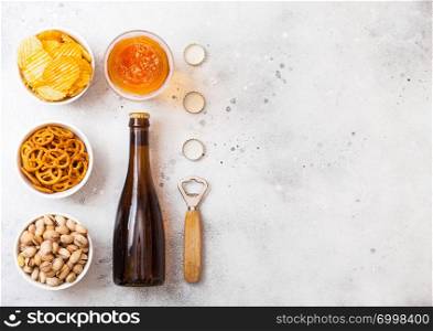 Glass and bottle of craft lager beer with snack on stone kitchen background. Pretzel and crisps and pistachio in white ceramic bowl