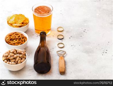 Glass and bottle of craft lager beer with snack on stone kitchen background. Pretzel and crisps and pistachio in white ceramic bowl.