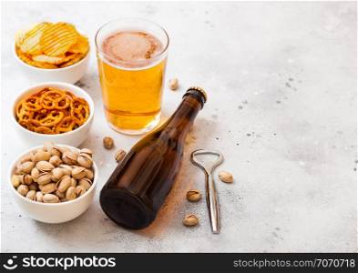 Glass and bottle of craft lager beer with snack on stone kitchen background. Pretzel and crisps and pistachio in white ceramic bowl.