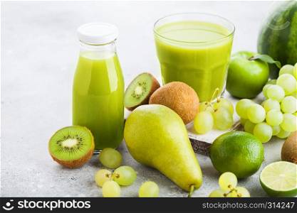 Glass and bottle of fresh smoothie with organic green toned fruits on stone kitchen table background. Pear and grapes with kiwi and lime with apple.