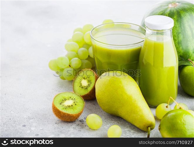 Glass and bottle of fresh smoothie with organic green toned fruits on stone kitchen table background. Pear and grapes with kiwi and lime with apple.