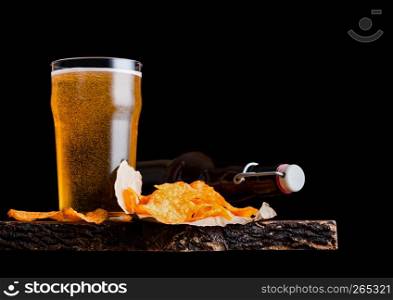 Glass and bottle of lager beer with potato crisps snack on vintage wooden board on black background.