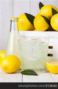Glass and bottle of organic fresh lemon juice with raw lemons in white wooden box