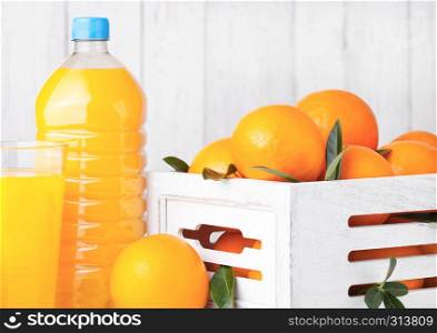 Glass and bottle of organic fresh orange smoothie juice with raw oranges in white wooden box