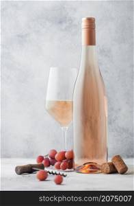 Glass and bottle of pink rose wine with grapes and corkscrew on light table background.