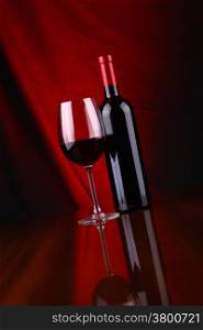 Glass and bottle of red wine over a draped background lit red