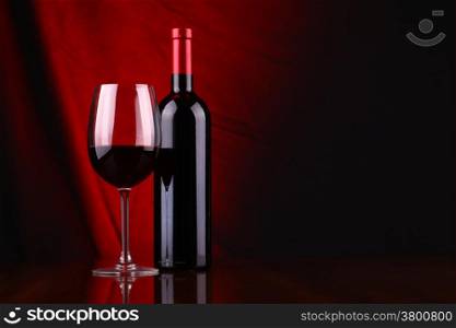 Glass and bottle of red wine over a draped background lit red