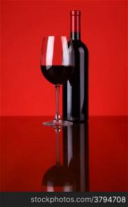 Glass and bottle of red wine over a red background