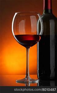 Glass and bottle of red wine over dark red background