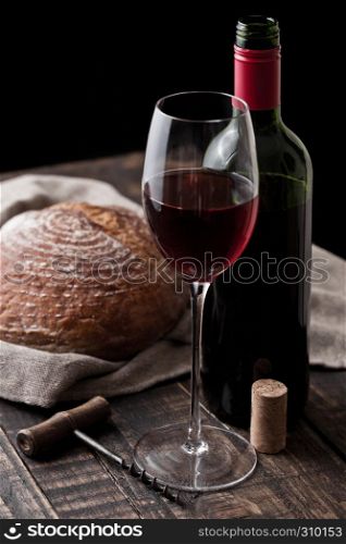 Glass and bottle of red wine with fresh loaf of bread with retro corkscrew in kitchen on wooden table