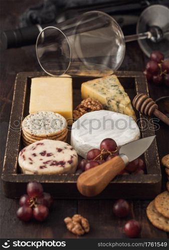 Glass and bottle of red wine with selection of various cheese in wooden box and grapes on wooden background. Blue Stilton, Red Leicester and Brie Cheese and knife.