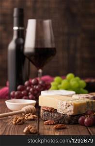Glass and bottle of red wine with selection of various cheese on the board and grapes on wooden table background. Blue Stilton, Red Leicester and Brie Cheese and knife.