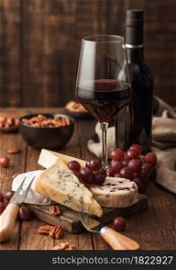 Glass and bottle of red wine with selection of various cheese on the board and grapes on wooden table background. Blue Stilton, Red Leicester and Brie Cheese and knife.