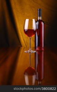 Glass and bottle of rose wine over a draped background lit yellow