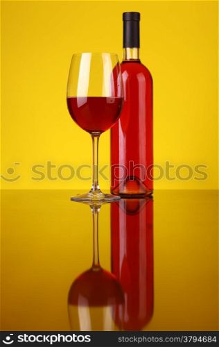 Glass and bottle of rose wine over a yellow background