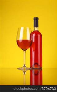 Glass and bottle of rose wine over a yellow background