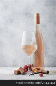 Glass and bottle of summer pink rose wine with grapes, corks and corkscrew on light table background.