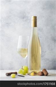 Glass and bottle of summer white wine with grapes, corks and corkscrew on light stone background.
