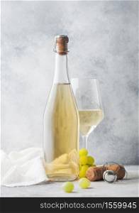 Glass and bottle of white homemade wine with grapes and corkscrew with linen cloth on light table background.