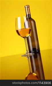 Glass and bottle of white wine over a yellow background
