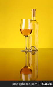 Glass and bottle of white wine over a yellow background