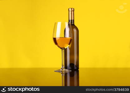 Glass and bottle of white wine over a yellow background