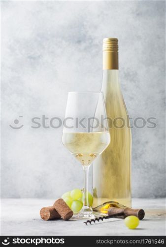 Glass and bottle of white wine with grapes and corkscrew on light table background.