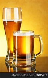 Glass and mug of beer over yellow background