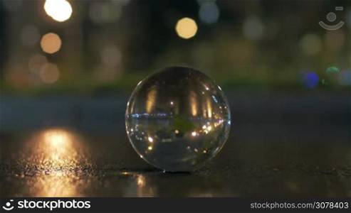 Glass ball on the asphalt and night city with car traffic reflecting in it