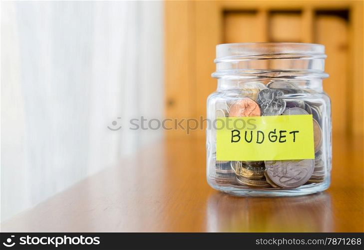 Glass bank with many world coins and budget word or label on saving money jar