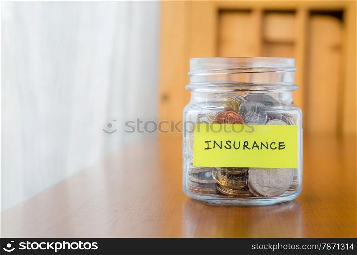 Glass bank with many world coins and insurance label on saving jar over table