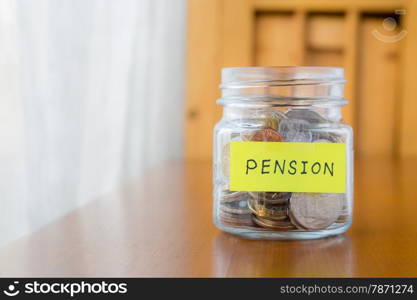 Glass bank with many world coins and pension word or label on money jar over table