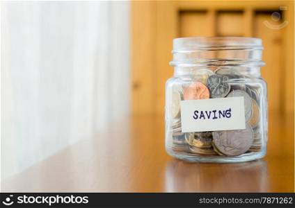 Glass bank with many world coins and saving word or label on money jar, concept to financial planning