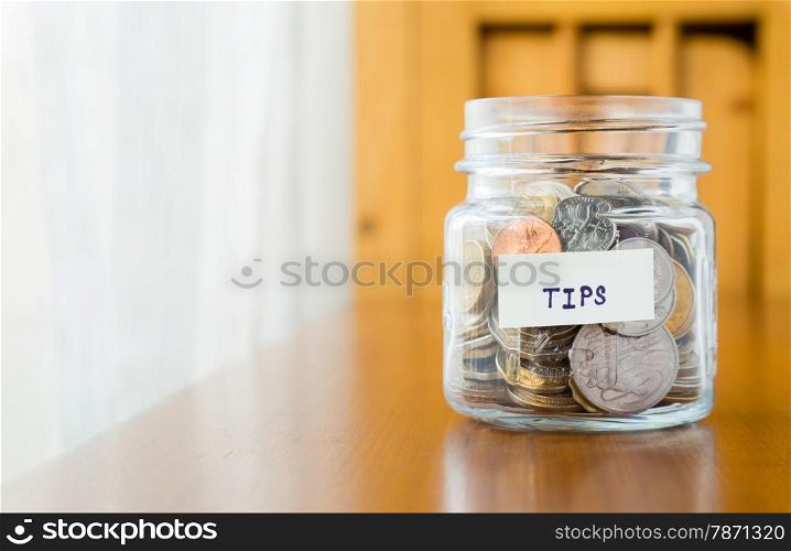 Glass bank with many world coins and tips word or label on saving money jar